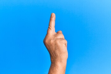 Hand of senior hispanic man over blue isolated background showing provocative and rude gesture doing fuck you symbol with middle finger