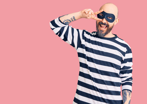 Young handsome man wearing burglar mask doing peace symbol with fingers over face, smiling cheerful showing victory