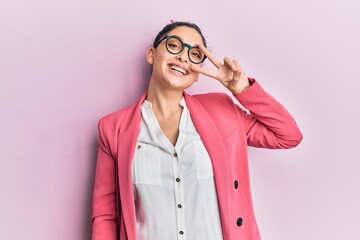 Beautiful middle eastern woman wearing business jacket and glasses doing peace symbol with fingers over face, smiling cheerful showing victory