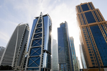 Fototapeta na wymiar 7 gratte-ciel ou buildings de Dubaï se dressant vers le ciel bleu. Nouveaux bâtiments vitrés à l'architecture moderne, présentant diverses lignes et courbes géométiques au soleil couchant et brillant.