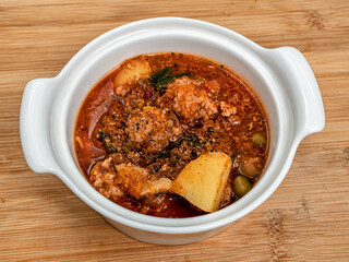 A pot full of homemade stewed vegetables ragout with mushrooms and meatballs on the wooden table. Close-up.
