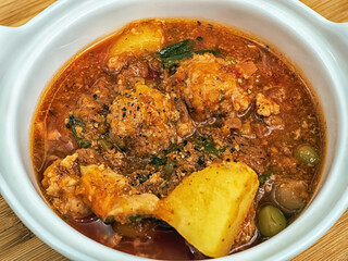 A pot full of homemade stewed vegetables ragout with mushrooms and meatballs on the wooden table. Close-up.
