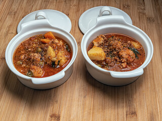 Two pots full of homemade stewed vegetables ragout with mushrooms and meatballs on the wooden table. Pot lids. Close-up.