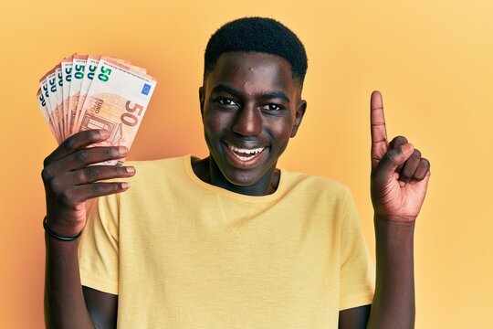 Young african american man holding 50 euro banknotes smiling with an idea or question pointing finger with happy face, number one