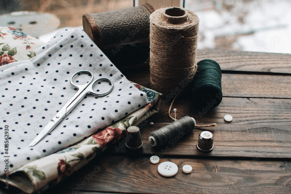 Wall mural Needlework concept. Various sewing tools. Needles, scissors, buttons, spools, threads of different colors. Sewing accessories and fabric. Sewing threads, needles, pins, fabric on a wooden background.