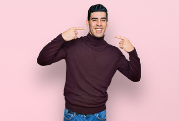 Handsome hispanic man wearing casual turtleneck sweater smiling cheerful showing and pointing with fingers teeth and mouth. dental health concept.