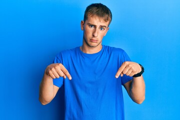 Young caucasian man wearing casual blue t shirt pointing down looking sad and upset, indicating direction with fingers, unhappy and depressed.