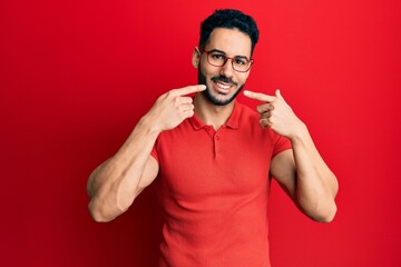 Young hispanic man wearing casual clothes and glasses smiling cheerful showing and pointing with fingers teeth and mouth. dental health concept.