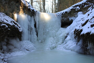 eiszeit im winter mit schnee in der landschaft und im wald eingeforener wasserfall mit eiszapfen...