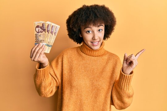 Young hispanic girl holding 5000 hungarian forint banknotes smiling happy pointing with hand and finger to the side