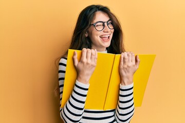 Young caucasian woman reading a book wearing glasses winking looking at the camera with sexy...