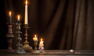 antique candlestick with burning candle on old wooden table on background brown velvet curtain - obrazy, fototapety, plakaty