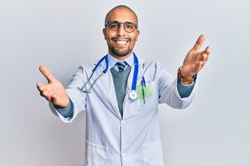 Hispanic adult man wearing doctor uniform and stethoscope looking at the camera smiling with open arms for hug. cheerful expression embracing happiness.