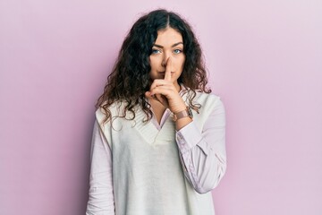 Young brunette woman with curly hair wearing casual clothes asking to be quiet with finger on lips. silence and secret concept.