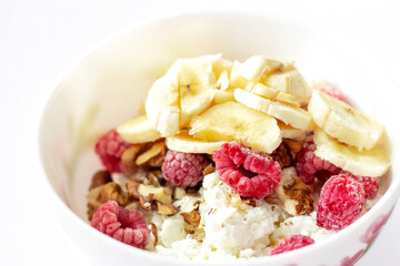 Close-up of a healthy breakfast with fruit in a white bowl. Cottage cheese with banana, raspberries and walnuts