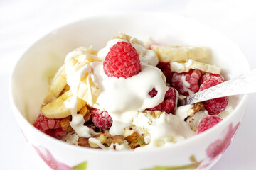 Close-up of a healthy breakfast with fruit in a white bowl with a spoon. Cottage cheese with banana, raspberries and walnuts