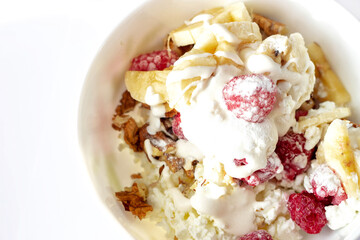 Close-up of a healthy breakfast with fruit in a white bowl. Cottage cheese with banana, raspberries, yogurt and walnuts