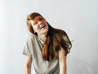 Happy laughing long-haired redhead young woman in a casual T-shirt on a white background.