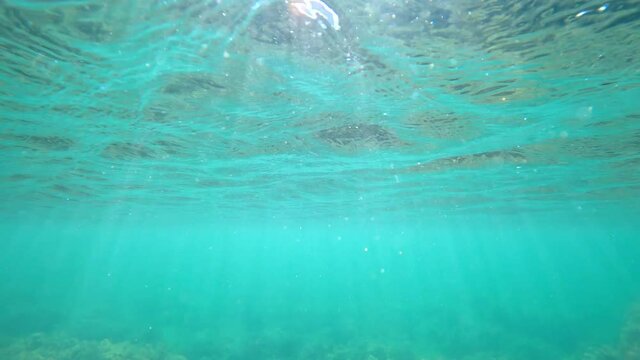 Waves underwater with sun rays. Transparent water with surface in ocean