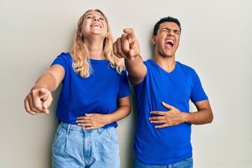 Young interracial couple wearing casual clothes laughing at you, pointing finger to the camera with hand over body, shame expression