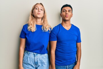 Young interracial couple wearing casual clothes looking at the camera blowing a kiss on air being lovely and sexy. love expression.