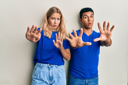Young interracial couple wearing casual clothes doing stop gesture with hands palms, angry and frustration expression