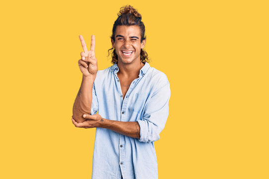 Young hispanic man wearing summer style smiling with happy face winking at the camera doing victory sign with fingers. number two.