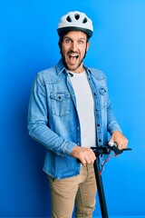 Young handsome man standing on modern scooter wearing helmet celebrating crazy and amazed for success with open eyes screaming excited.