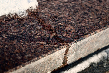 polished granite surface with slowly melting snow / purple brown smooth shiny stone 
