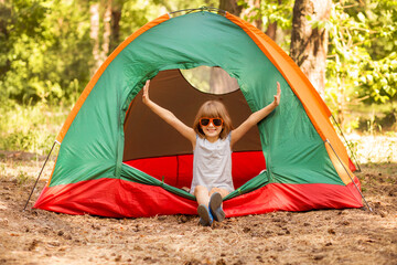 happy child girl in camp tent enjoy forest holidays with hands up.