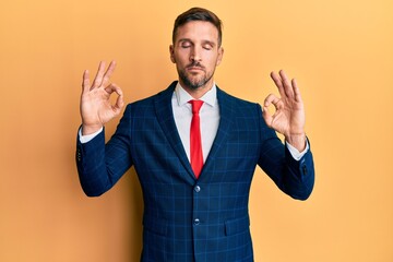 Handsome man with beard wearing business suit and tie relax and smiling with eyes closed doing meditation gesture with fingers. yoga concept.