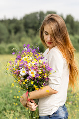 Naklejka na ściany i meble beautiful young girl with long hair in a field with a bouquet of flowers.