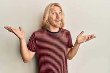 Caucasian young man with long hair wearing casual striped t shirt clueless and confused with open...