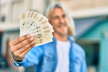 Young blond scandinavian man smiling happy holding danmark 100 kroner banknotes at the city.