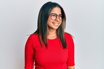 Young latin girl wearing casual clothes and glasses looking to side, relax profile pose with...