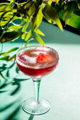 red tropical cocktail with ice in the form of a crystal on a background of foliage and shadows from sunlight.Green background