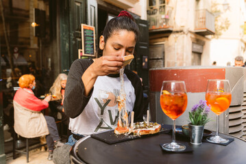 young woman eating italian bruschetta with stringy mozzarella cheese doing italian happy hour with spritz drink known as aperitivo in bar terrace