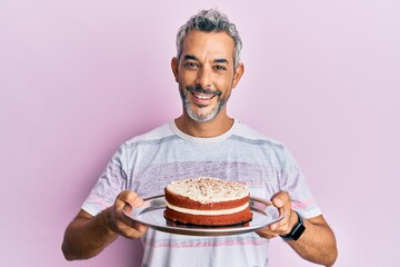 Middle age grey-haired man holding carrot cake smiling with a happy and cool smile on face. showing teeth.