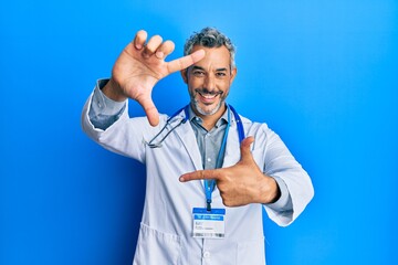 Middle age grey-haired man wearing doctor uniform and stethoscope smiling making frame with hands...