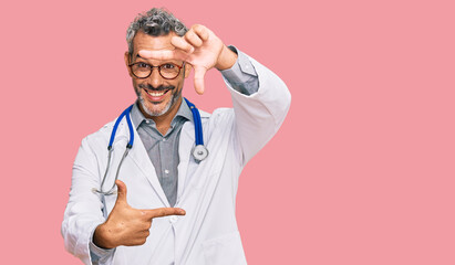Middle age grey-haired man wearing doctor uniform and stethoscope smiling making frame with hands and fingers with happy face. creativity and photography concept.