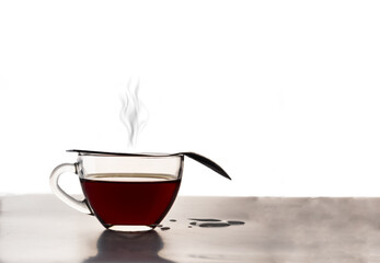 Transparent glass cup with tea and a teaspoon. Steam rises from the hot tea. Isolated on a white background