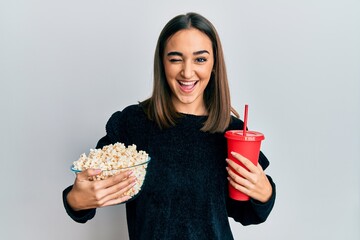Young brunette girl eating popcorn and drinking soda winking looking at the camera with sexy...
