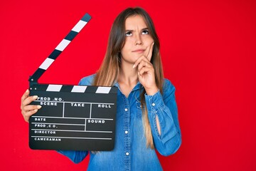 Beautiful caucasian woman holding video film clapboard serious face thinking about question with...
