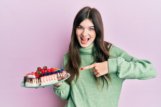 Young beautiful caucasian girl holding cake slices smiling happy pointing with hand and finger