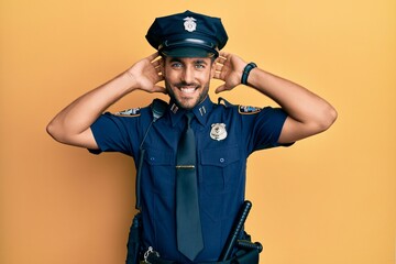 Handsome hispanic man wearing police uniform relaxing and stretching, arms and hands behind head and neck smiling happy