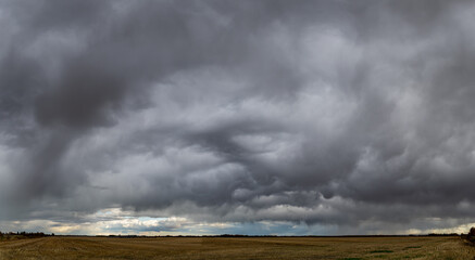 Dramatic gray storm clouds over a panoramic prairie landscape.
