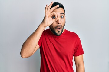 Fototapeta na wymiar Young hispanic man wearing casual clothes doing ok gesture shocked with surprised face, eye looking through fingers. unbelieving expression.
