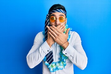 Young hispanic businessman wearing party funny style with tie on head shocked covering mouth with hands for mistake. secret concept.