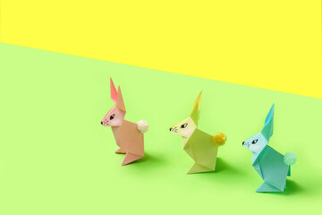 Paper Easter bunnies-origami made of colored paper on a bright yellow-green background. The concept of the celebration of Easter, greeting card, crafts with your own hands.