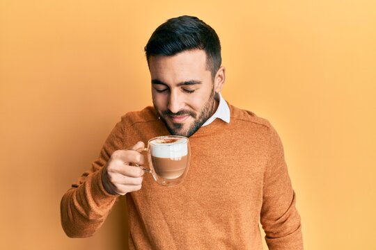 Handsome hispanic man enjoying a cup of coffee over yellow background